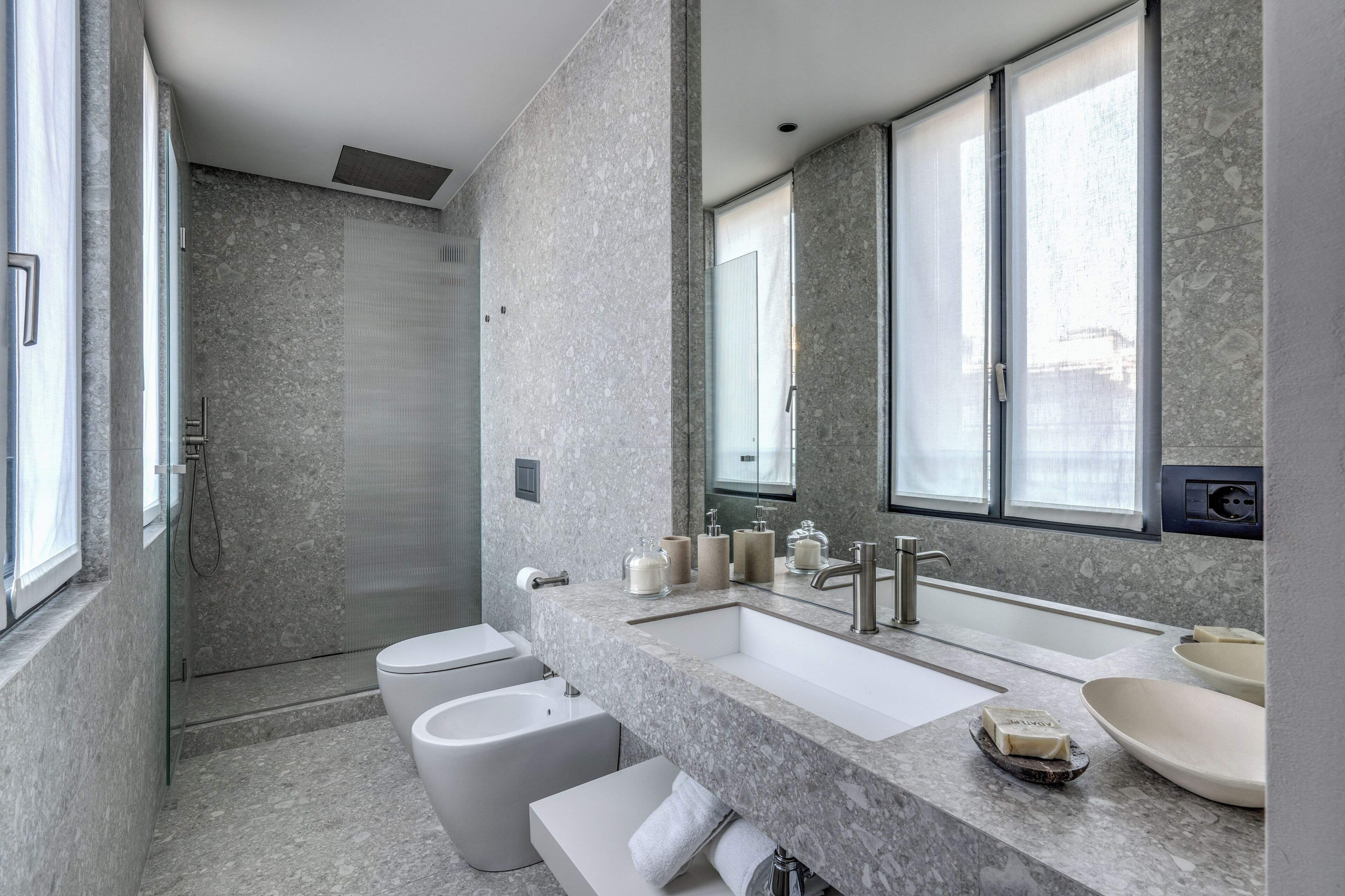 Une salle de bain moderne avec un grand lavabo, deux toilettes, une douche et un grand miroir.