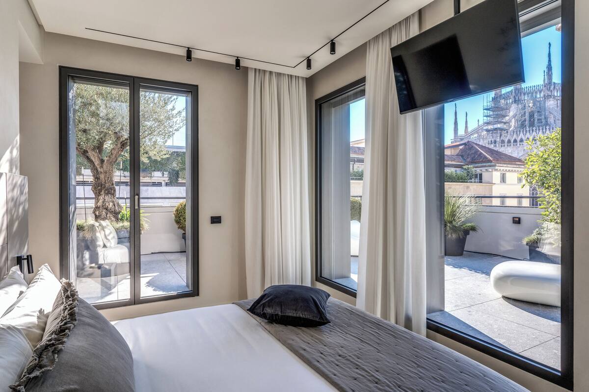 A modern hotel room with a large bed, a TV mounted on the wall, and a view of a cathedral through the window.