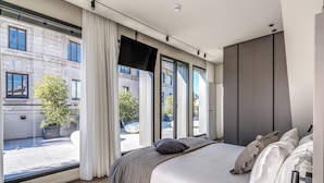 Quarto moderno com uma cama grande, uma televisão e vista para a rua.