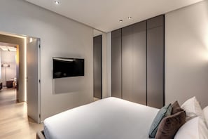 Quarto moderno com cama grande, televisão de tela plana na parede e guarda-roupa com portas deslizantes.