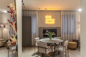 Uma sala de estar moderna com uma mesa de jantar redonda, assentos confortáveis, uma televisão de tela plana e um letreiro de neon na parede.