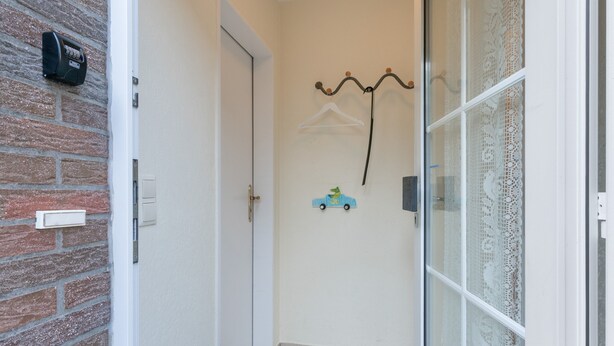 Ein Flur mit einer Tür, einem Kleiderhaken mit Kleiderbügeln, einem kleinen blauen Spielzeugauto und einem Briefkasten an der Wand.