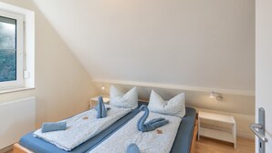 Ein Zimmer mit zwei Betten, einem Fenster, einem Nachttisch und einer Lampe.