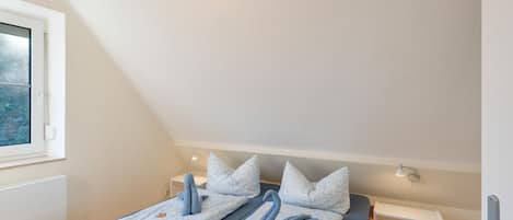Ein Zimmer mit zwei Betten, einem Fenster, einem Nachttisch und einer Lampe.