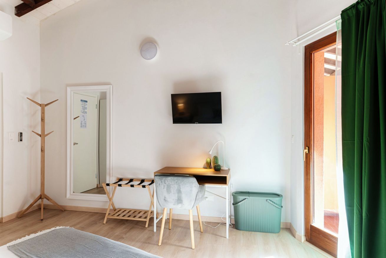 A room with a desk, chair, TV, and a green trash bin.