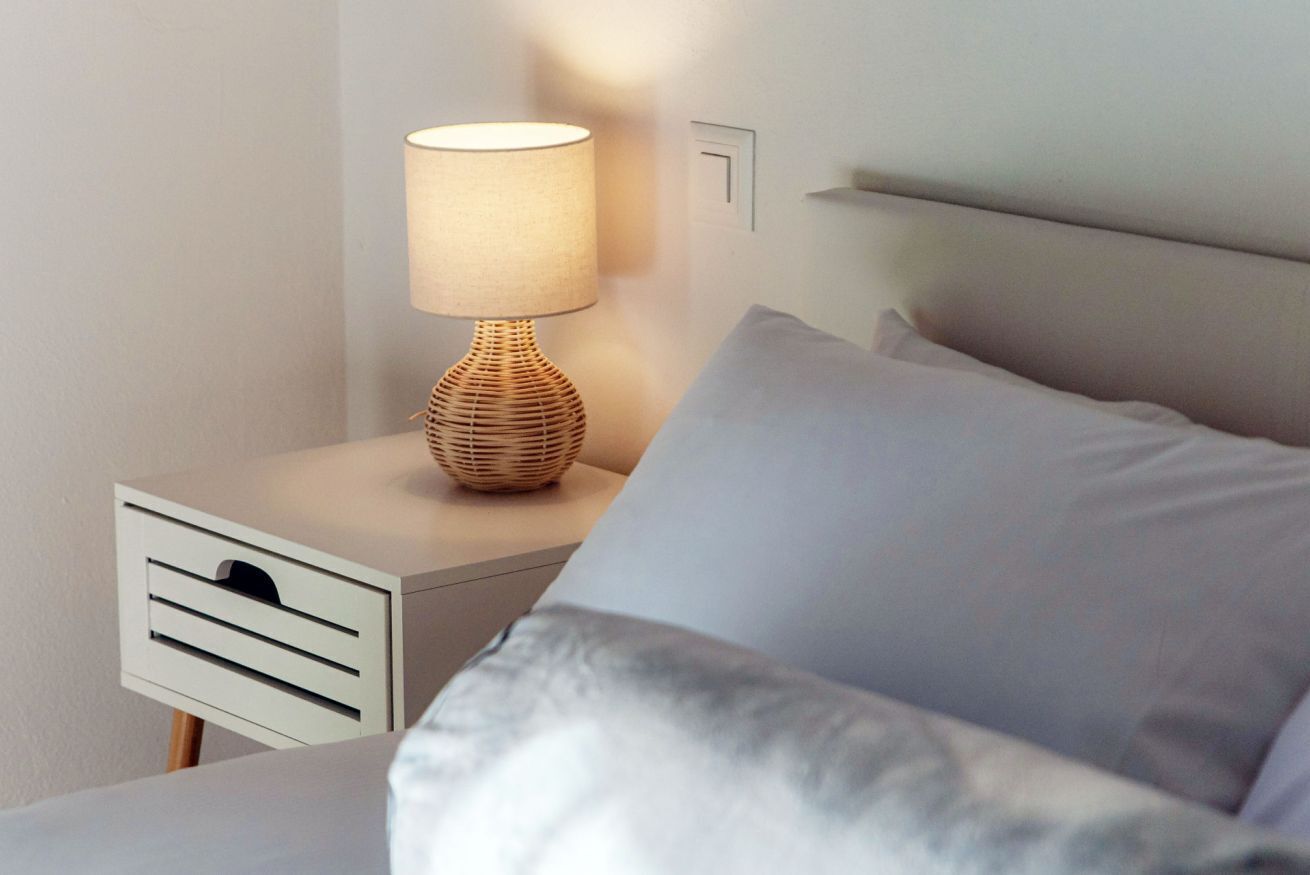 A bed with a white headboard, a bedside table with a lamp, and a drawer unit.