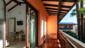 A balcony with a table and chairs, a sliding glass door leading to a room with a desk and chair, and a view of a building and palm trees. - <p><strong>Near the lake and the center (FLORIDA ASCONA Room 12)</strong></p><p>Just a few steps from the center and the charming lakeside promenade of Ascona, FLORIDA ASCONA Room 12 welcomes guests into a refined and comfortable setting, ideal for disco (Ascona)