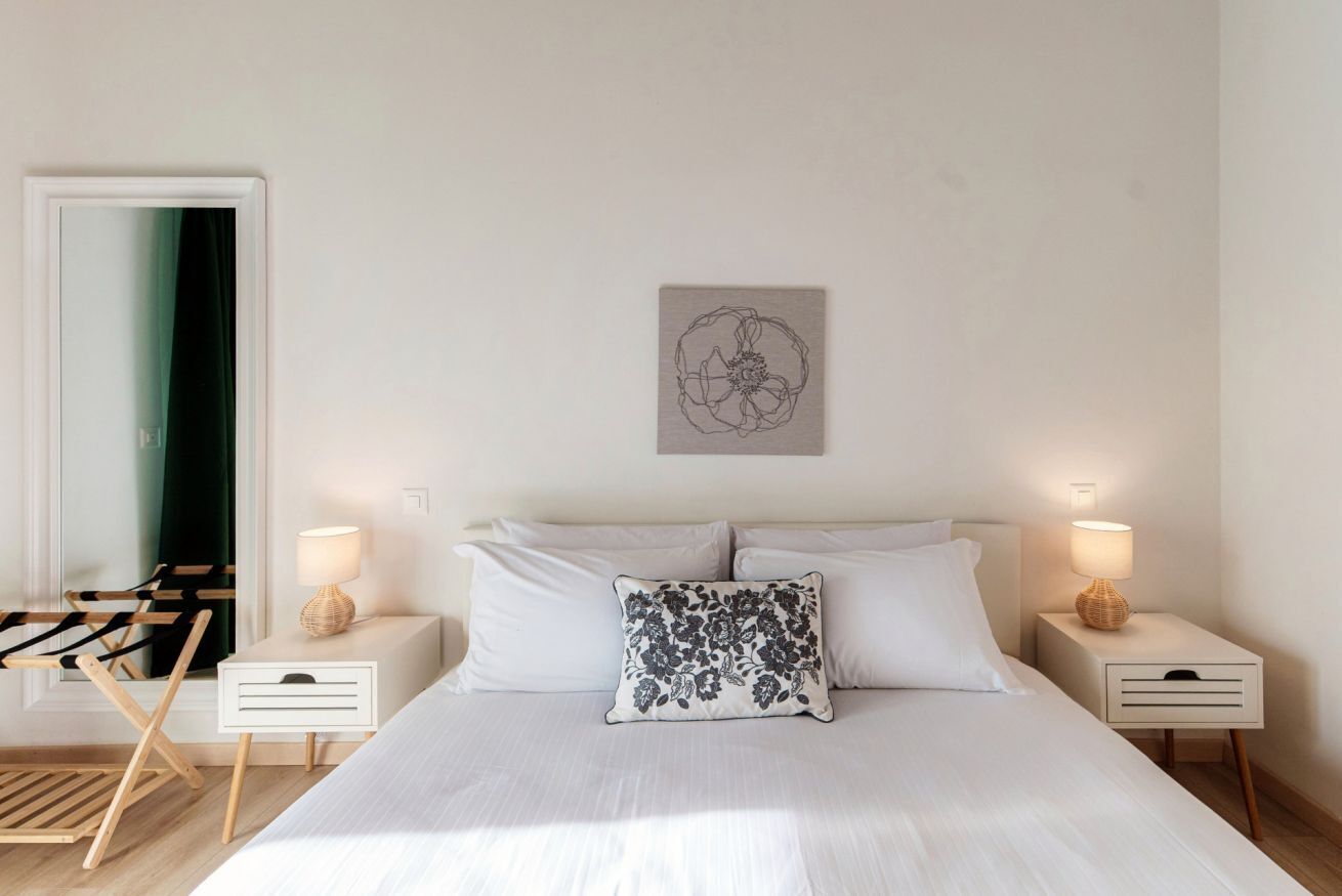 A bedroom with a bed, two bedside tables with lamps, a wall-mounted artwork, and a chair with a mirror.