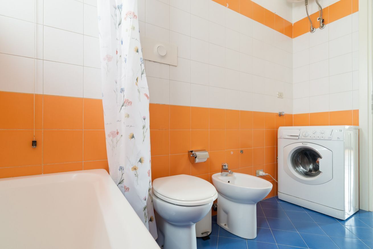 Une salle de bain avec une baignoire, deux toilettes, un bidet et un lave-linge.