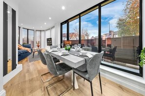 Uma zona de refeições moderna com uma janela ampla, um sofá e uma mesa de jantar posta para quatro pessoas.