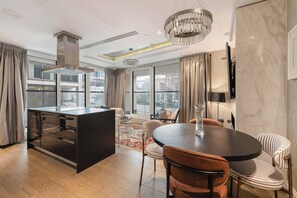 A modern kitchen with a central island, a dining area with a round table and striped chairs, and large windows offering a city view. - Luxury Kensington Home - Concierge Elevator AC (London)