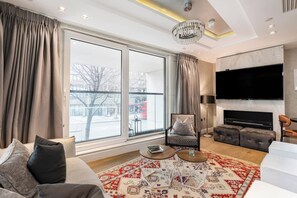 A modern living room with a large window, a sofa, a chair, a coffee table, and a TV. - Luxury Kensington Home - Concierge Elevator AC (London)