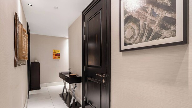 Un couloir avec une porte noire, un tableau abstrait encadré, une petite table avec un bol et une affiche accrochée au mur.