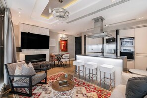A modern living room with a sofa, TV, and a dining area with chairs and a table. - Luxury Kensington Home - Concierge Elevator AC (London)