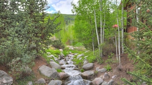 A natural stream flowing through a forested area with large rocks and trees, leading to a building with a red roof. - Prime Location, Steps from the Ski Lift - 2 Bedroom Condo in Arrowhead Village 2 Condo (Edwards)