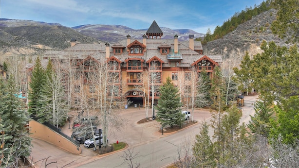 A large, multi-story building with a prominent tower and multiple chimneys, surrounded by trees and set against a mountainous backdrop. - Prime Location, Steps from the Ski Lift - 2 Bedroom Condo in Arrowhead Village 2 Condo (Edwards)