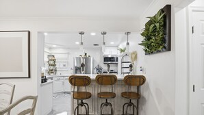 A modern kitchen with white cabinetry, a central island with bar stools, and pendant lighting. - Suite Retreat (Severn)