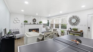 A modern living room with a ping pong table, a fireplace, and a large window with blinds. - Suite Retreat (Severn)