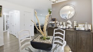 A dining area with a glass table, chairs, a decorative plant, a coffee machine, and a mirror on the wall. - Suite Retreat (Severn)