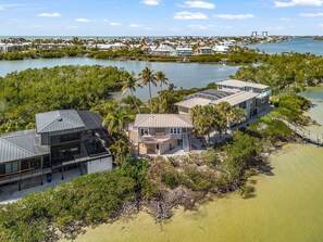 A coastal property with multiple buildings, including a large house with a balcony and a smaller structure with a sloped roof. - 21381 Widgeon Point 6 Bedroom Estate (Fort Myers Beach)