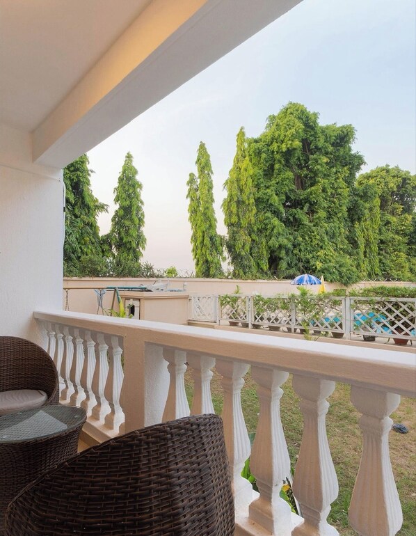 A balcony with wicker furniture, a white balustrade, and a view of trees and a pool. - Ceevu Ninteen Homestay (Port Harcourt)