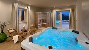 A modern indoor swimming pool with a wooden deck area, a glass-enclosed changing room, and a view of the outdoors. - Villa Ovi (Karojba)