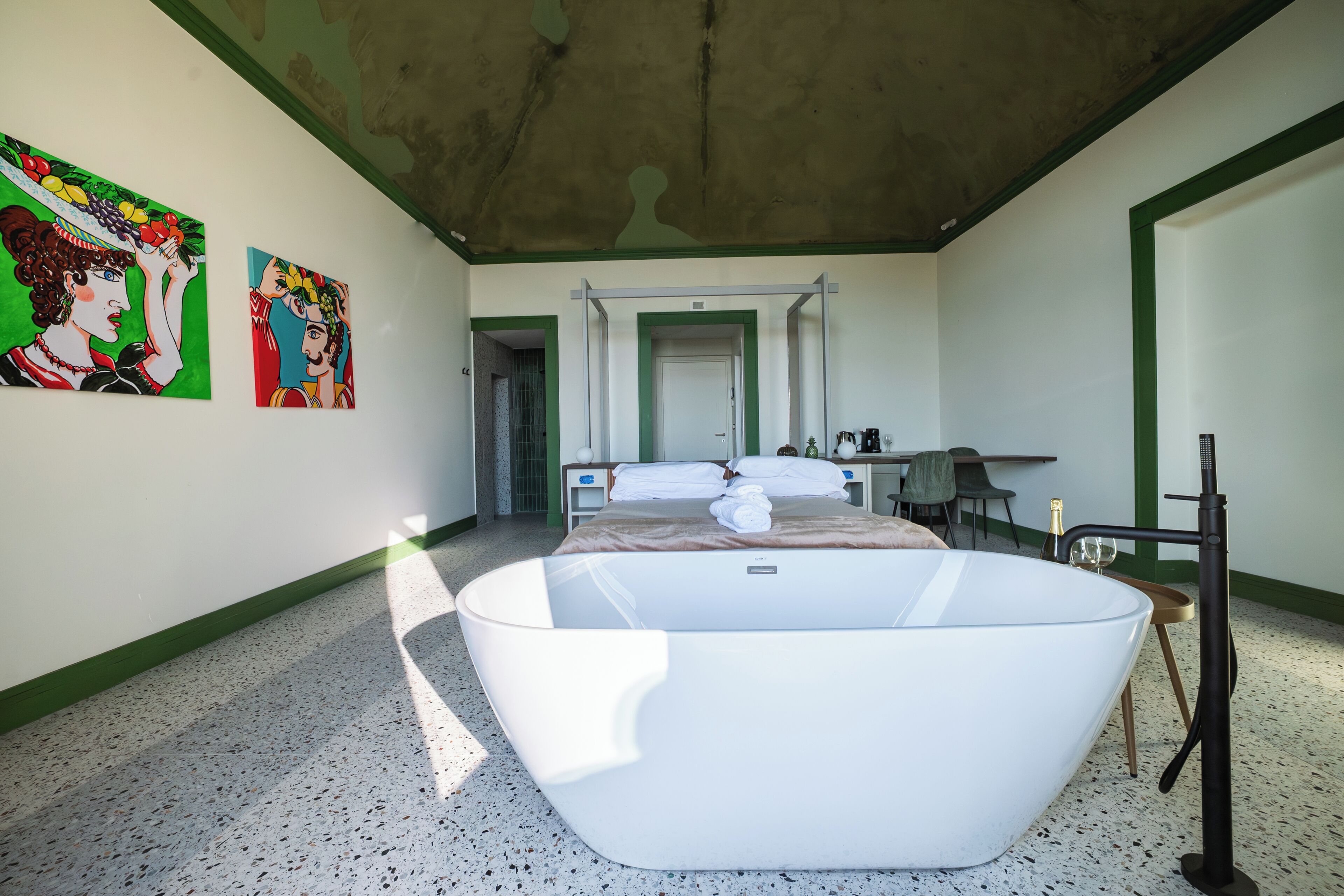 A modern bathroom with a freestanding bathtub, a large mirror, and two paintings on the wall.