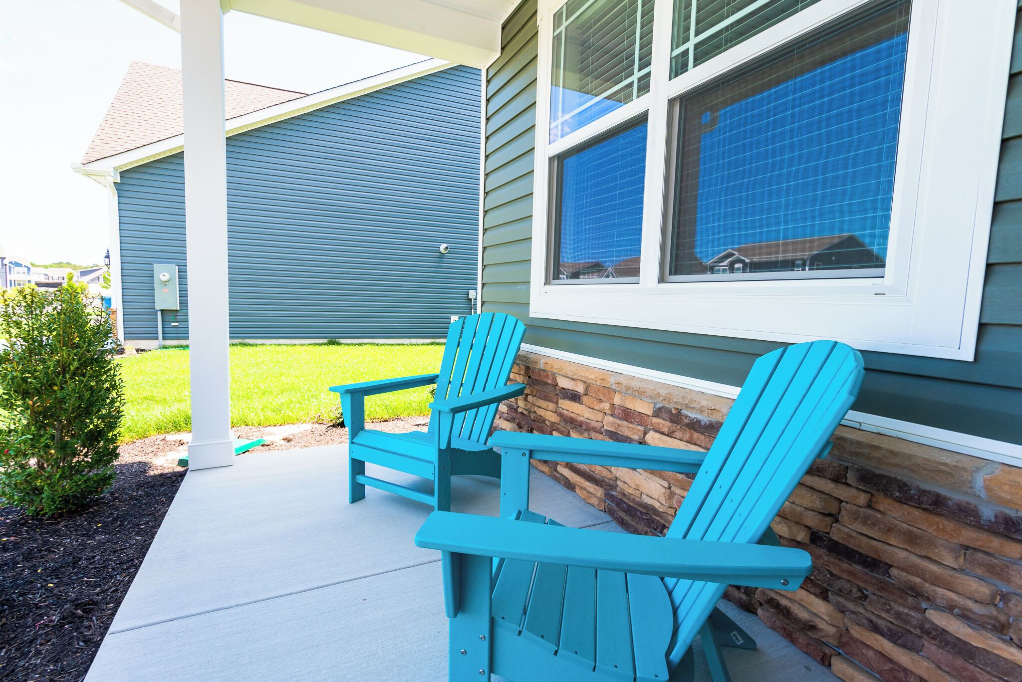 A covered porch with two turquoise Adirondack chairs and a stone wall.
