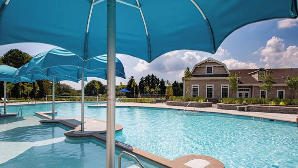 Une piscine avec des parasols bleus, un ciel dégagé et un bâtiment en arrière-plan.