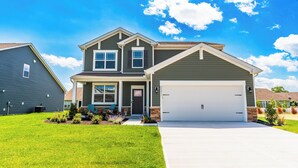Une maison à deux étages avec un garage, une pelouse bien entretenue et un ciel d’un bleu éclatant.