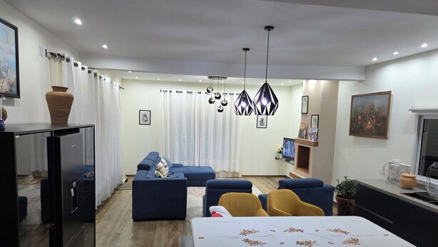 A modern living room with a sofa set, a dining table, and a kitchen area with a refrigerator.