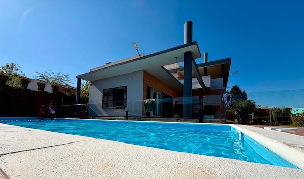 A modern house with a swimming pool, a garage, and a clear blue sky.