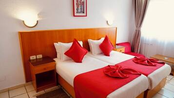 Une chambre d’hôtel avec deux lits, une literie rouge et blanche, une tête de lit en bois, des tables de chevet et des lampes fixées au mur.