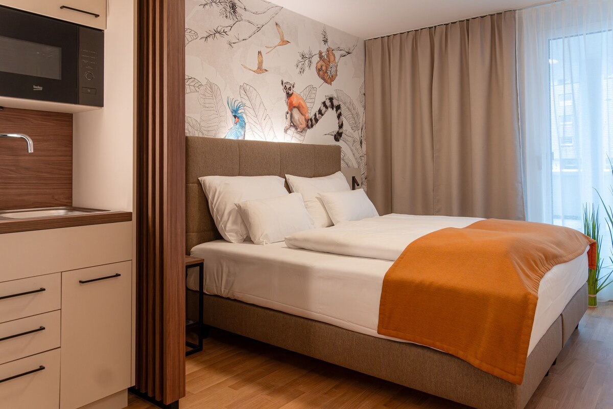 A modern hotel room with a bed, a built-in TV, and a wall mural.