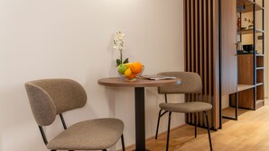 A dining area with two chairs, a table with a fruit bowl and a vase, and a wooden bookshelf. - OLIVER pulse I Self check-in Apartments (Vienna)