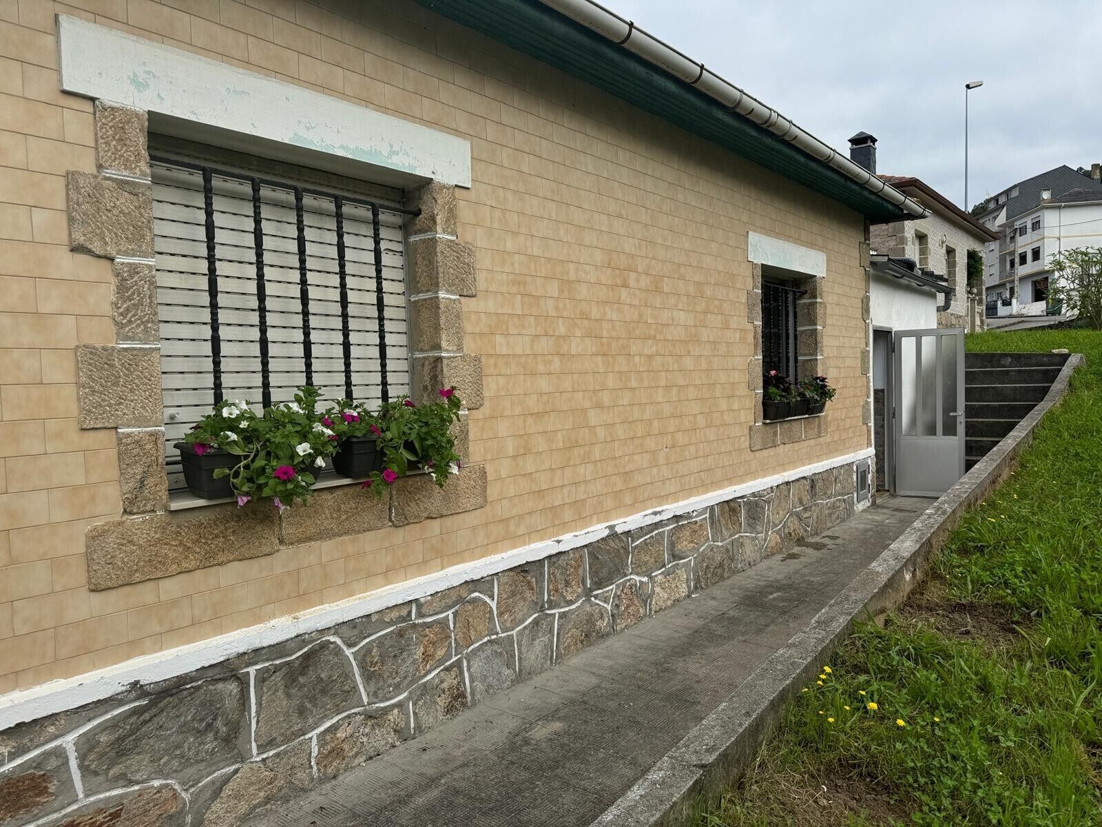 A building with a stone base, a beige brick upper section, a window with a metal grill, and a small window with a door.