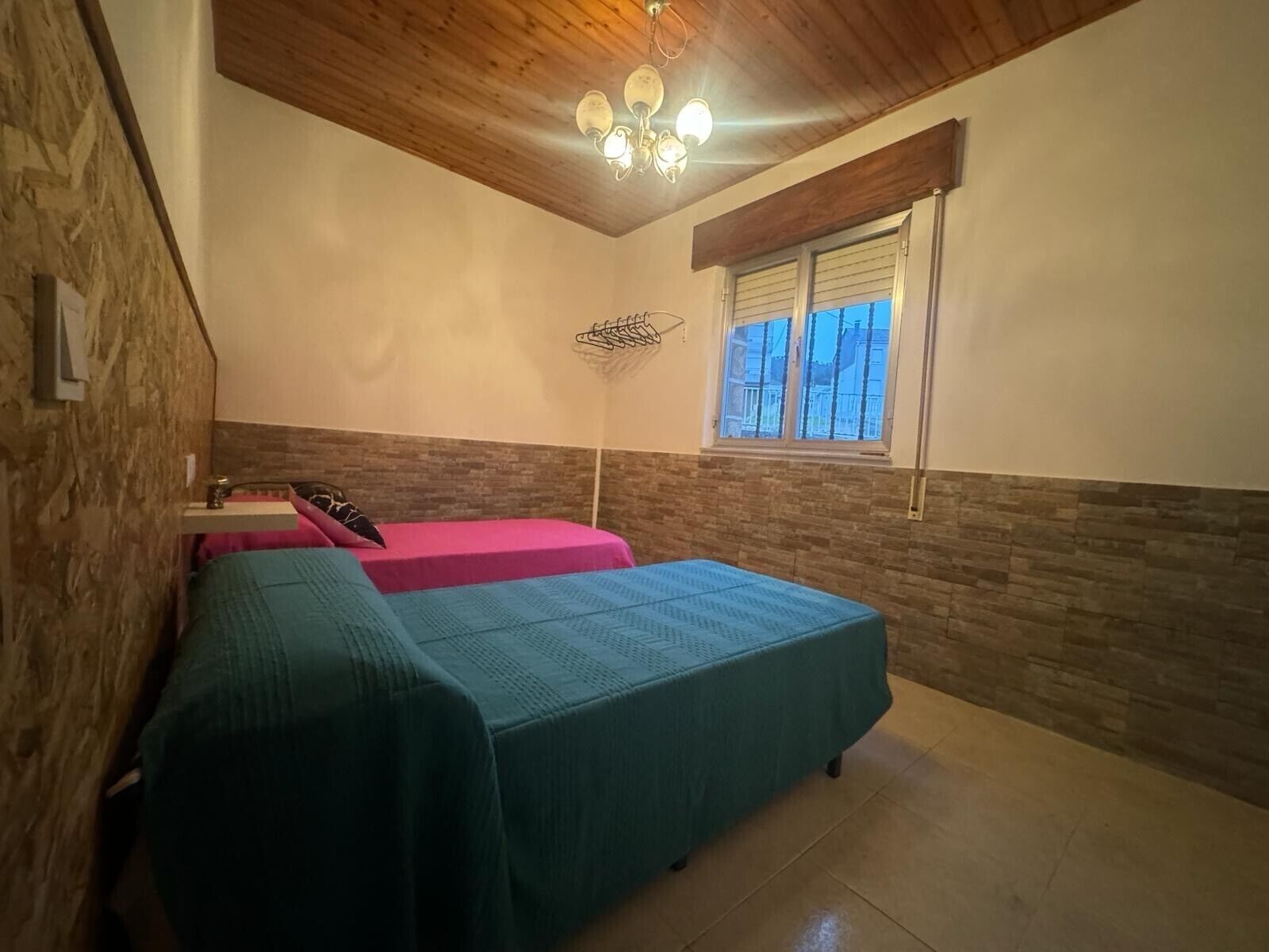 Een kamer met twee bedden, een houten plafond, een raam en een hanglamp.
