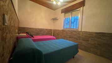 Een kamer met twee bedden, een houten plafond, een raam en een hanglamp.