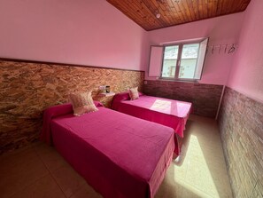 A room with two beds, a wooden ceiling, a window, and a brick wall.