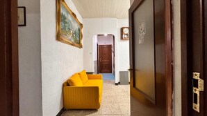 Um corredor com um sofá amarelo, uma porta de madeira, um radiador e um quadro pendurado na parede.