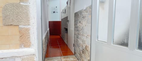 Un pasillo estrecho con suelo de baldosas, paredes de piedra y una puerta con ventanal.