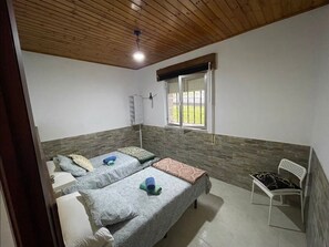 A room with two beds, a window, a chair, and a ceiling fan.