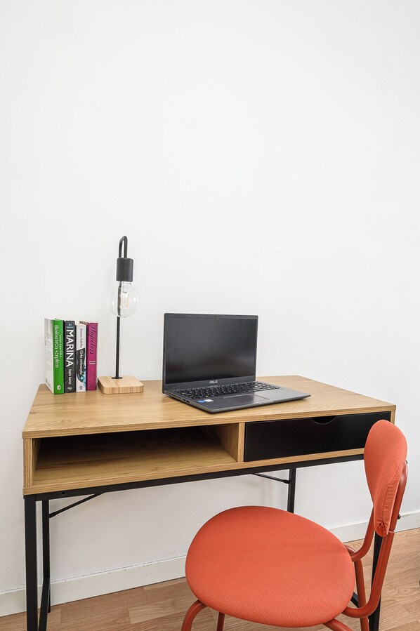 Een houten bureau met een laptop, een lamp en boeken.