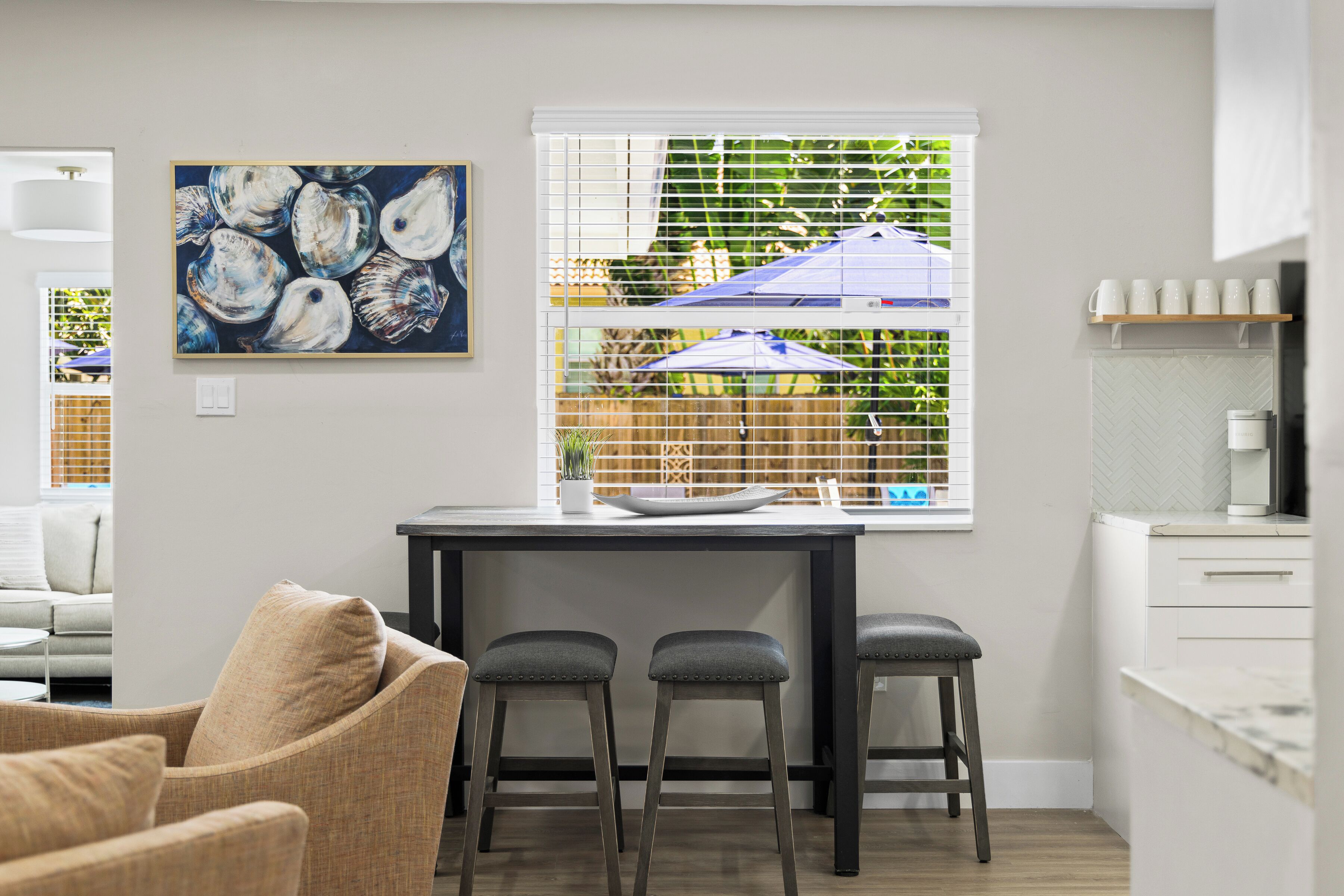 Une cuisine moderne avec un coin repas, un tableau accroché au mur et une fenêtre avec des stores.