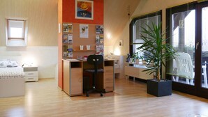 A modern bedroom with a wooden floor, a bed, a desk with a chair, a window with blinds, and a potted plant. - Apartment 'Eva Maria' with Shared Pool, Garden and Wi-Fi (Mahlberg)