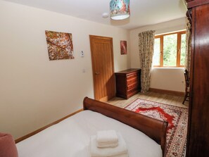 Un dormitorio con cama, cómoda de madera, puerta y ventana con cortinas.