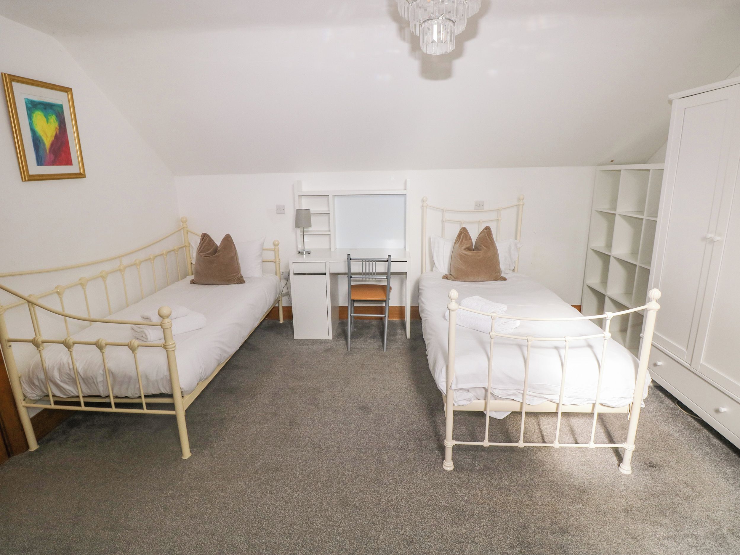 A room with two single beds, a desk, a chair, a wardrobe, and a ceiling light.
