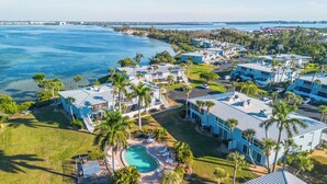 A coastal hotel with multiple buildings, a swimming pool, and palm trees. - West Bay Cove 213 · 3 Blks to Beach · 30-Night (Holmes Beach)