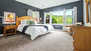 A bedroom with a large bed, two bedside tables, a nightstand, a dresser, and a window with curtains. - Grand Galena Hideaway [ Luxe Retreat w/ Hot Tub & Games ] (Galena)