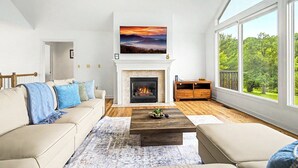A living room with a fireplace, a sofa, a coffee table, and a view of the outdoors. - Grand Galena Hideaway [ Luxe Retreat w/ Hot Tub & Games ] (Galena)